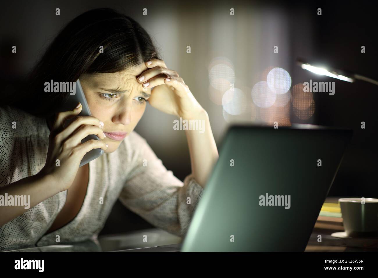 Besorgte Frau, die den Laptop überprüft und nachts telefoniert Stockfoto