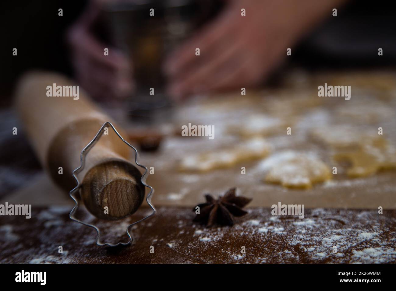 Ein weihnachtlicher, baumförmiger Schimmel, der sich auf eine Walznadel lehnt, vor einem Hintergrund aus Keksen, Pergament und Mehl, das aus Teig geschnitten wurde. Fotos in dunklen Farben. Stockfoto