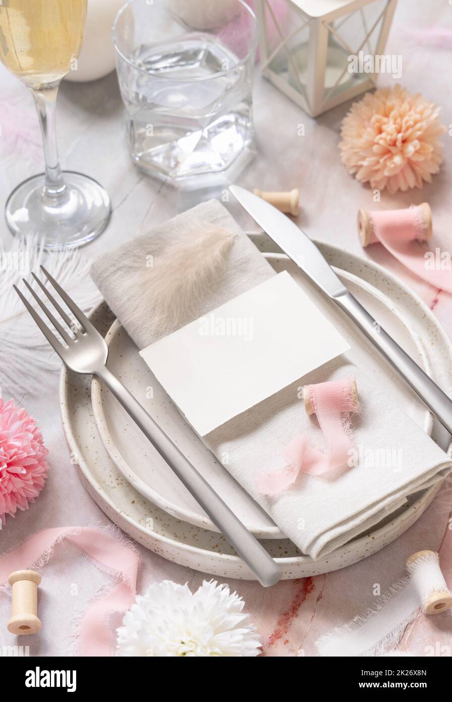 Hochzeitstisch mit einer Karte über der Serviette neben Blumen, Seidenbändern und Federn, Modell Stockfoto