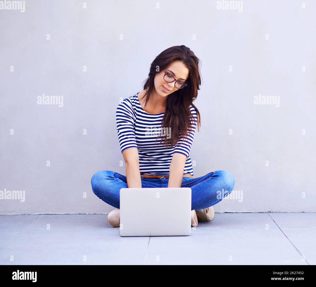Einfach in der Blog-o-sphere surfen. Ganzkörperaufnahme einer attraktiven jungen Frau, die mit einem Laptop auf gekreuzten Beinen sitzt. Stockfoto