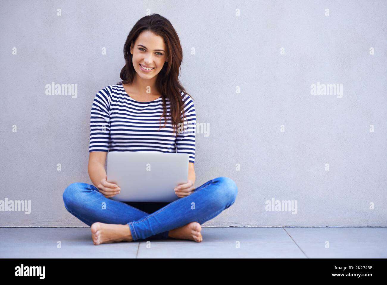 Einfach in der Blog-o-sphere surfen. Ganzkörperaufnahme einer attraktiven jungen Frau, die mit gekreuzten Beinen auf einem Laptop sitzt. Stockfoto