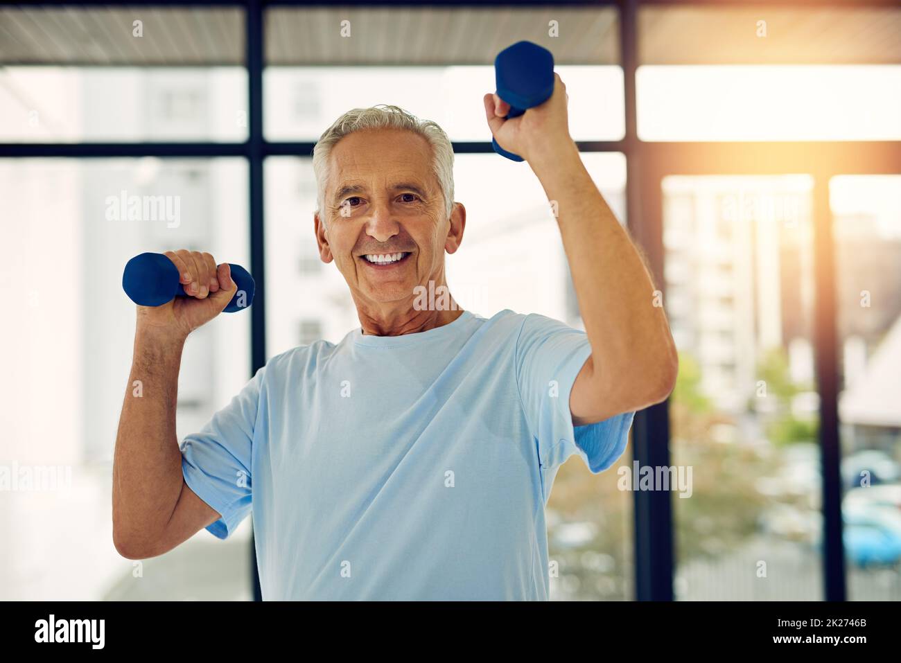 Aktiv zu bleiben bedeutet, gut zu altern. Porträt eines leisen und lächelnden Senioren beim Heben von Gewichten im Fitnesscenter. Stockfoto