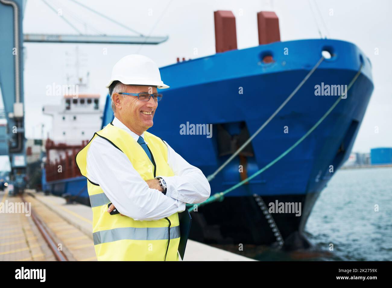 Ich liebe meinen Job. Ein zufriedener Hafenarbeiter, der inmitten der Schifffahrtstätigkeit am Hafen steht. Stockfoto