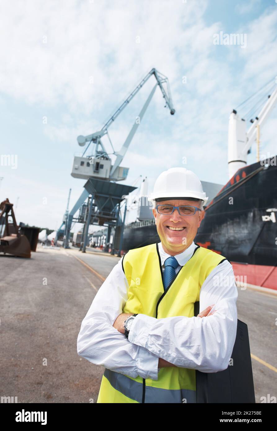 Meine Arbeit bringt mir enorme Freude. Porträt eines Hafenarbeiters, der inmitten der Schifffahrt am Hafen steht. Stockfoto