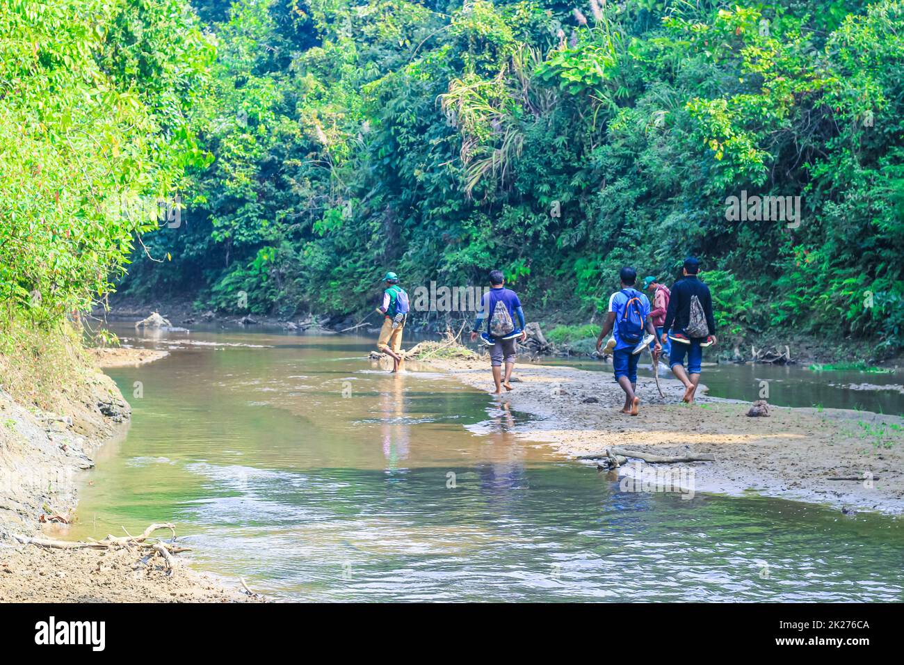 Mann, der mit den Schuhen in der Hand am Bach im Wald vorbeiläuft. Wanderer wandern im Wald. Gruppe von Wanderern, die im Wald spazieren. Stockfoto