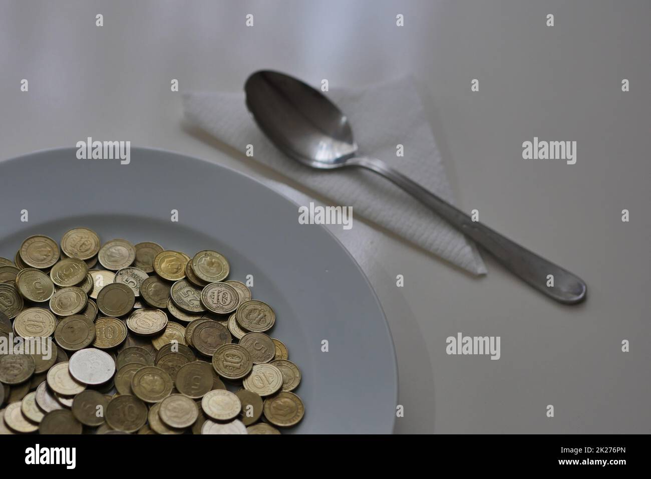 Ein Teller voller Münzen auf einem Tisch und ein Löffel daneben, Taschengeld Stockfoto