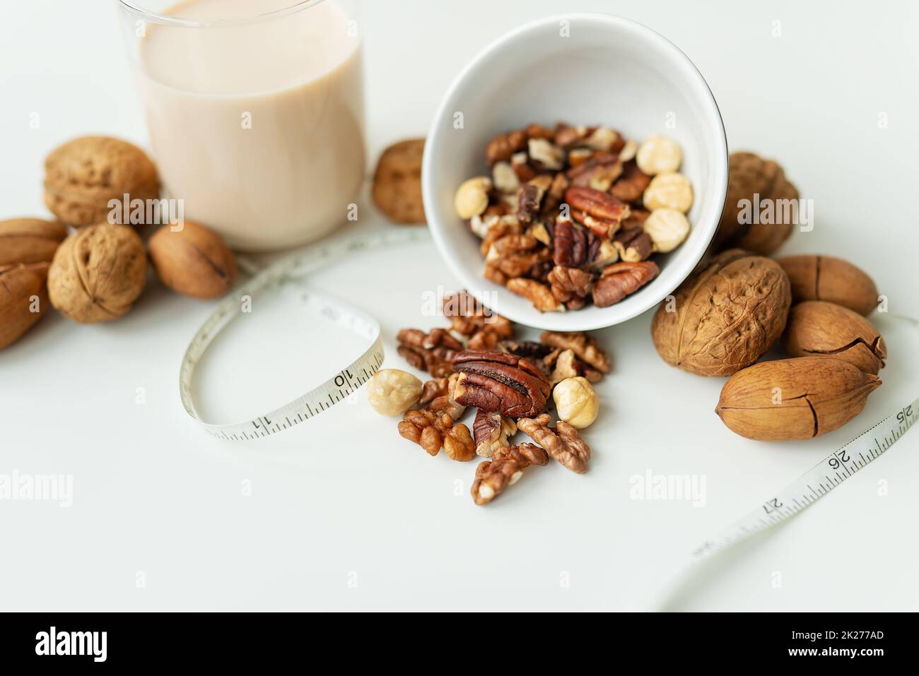 Vegane Milch aus Nüssen in einem Glasbecher mit verschiedenen Nüssen auf einem weißen Tisch. Nüsse in einer Schüssel. Kalorienarme Milch zur Unterstützung des Körpers. Stockfoto