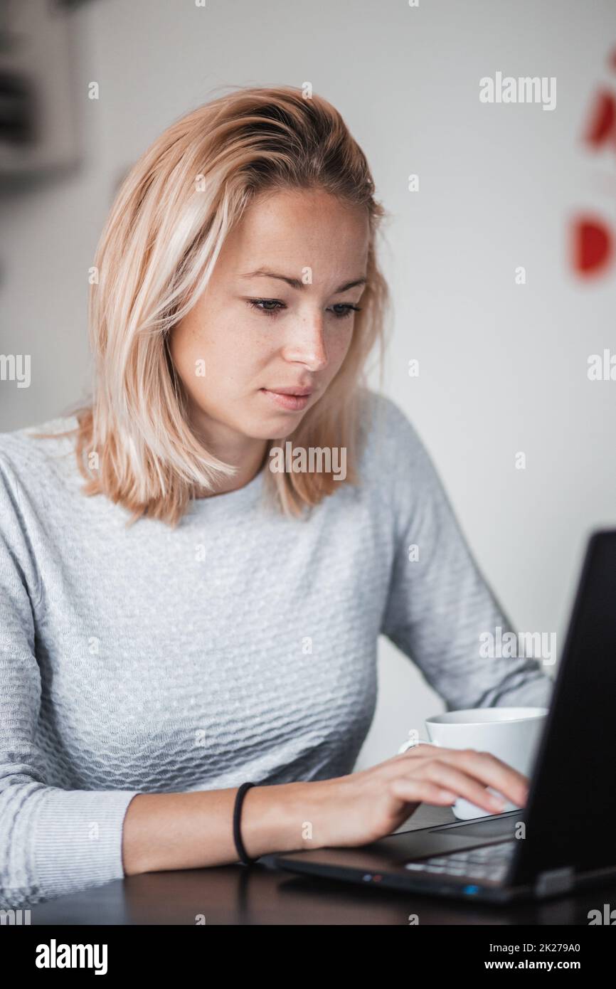 Weibliche Freiberufler in Ihrem beiläufigen home Kleidung arbeiten ferngesteuert von Ihrem Esstisch am Morgen. Home Küche im Hintergrund. Stockfoto