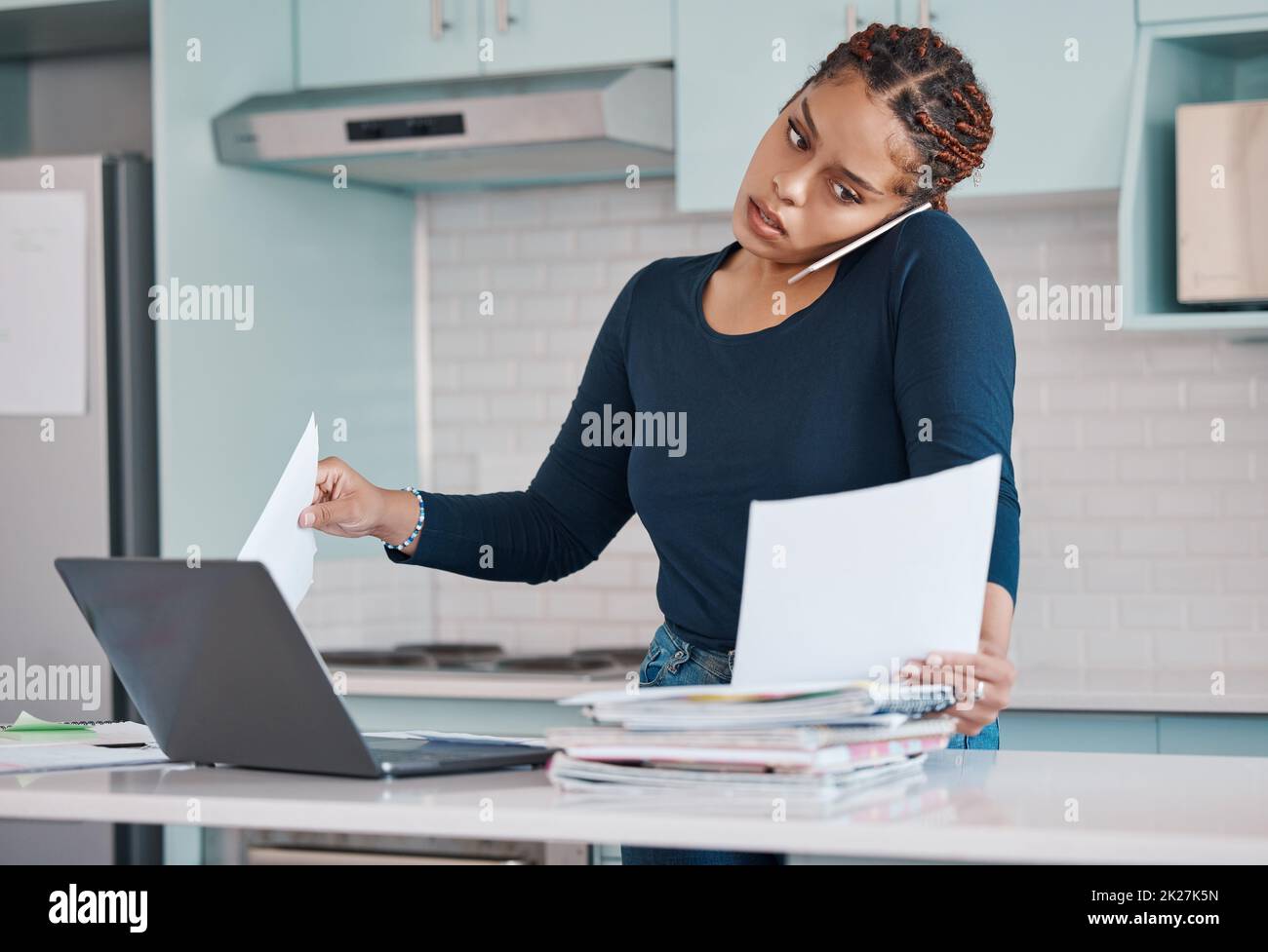 Schwarze Geschäftsfrau, die von zu Hause aus mit freiberuflicher, multitasking-Papierarbeit mit Laptop und Mobiltelefon-Audioanruf arbeitet. Internet-Technologie in der Küche Stockfoto