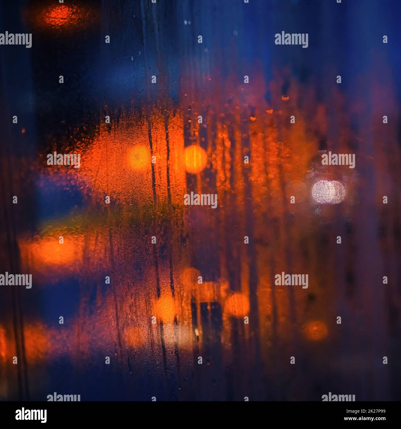 Feuchtes, dampfiges Fenster im Bus an einem regnerischen Tag, verschwommenes orangefarbenes und blaues Licht im Hintergrund - abstrakter, launischer Hintergrund Stockfoto