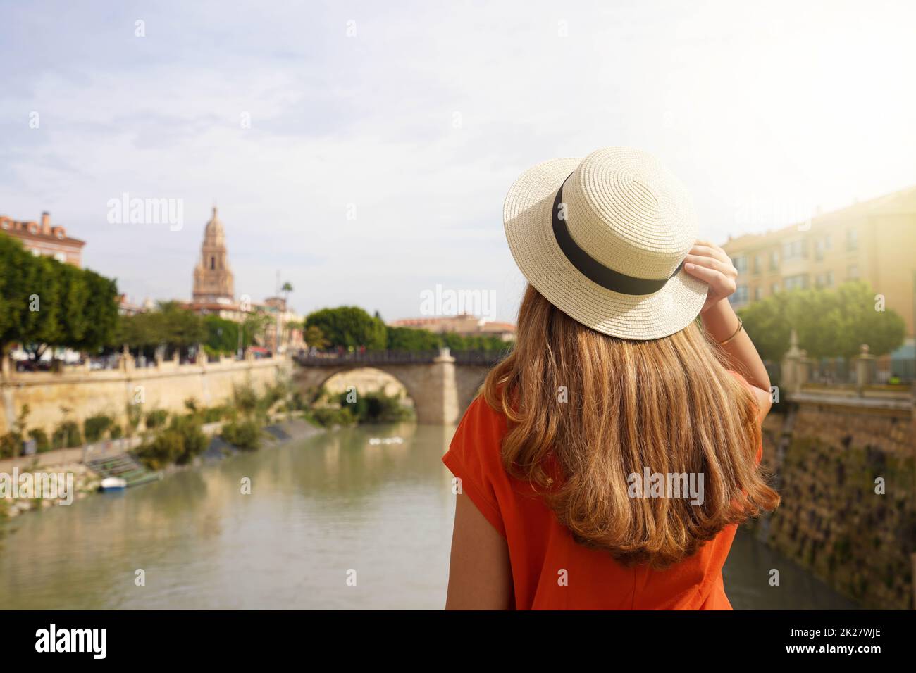 Besuch In Murcia, Spanien. Rückansicht eines touristischen Mädchens, das die Stadtlandschaft von Murcia mit der Puente Viejo Brücke und dem Glockenturm der Kathedrale, Spanien, genießt. Stockfoto
