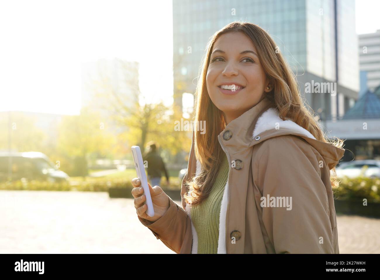 Lächelnd schönes Mädchen hält Smartphone draußen auf Sonnenuntergang Stockfoto