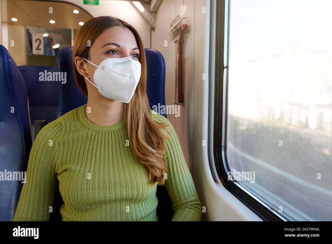 Student im öffentlichen Nahverkehr mit obligatorischer medizinischer Gesichtsmaske, die durch das Fenster schaut Stockfoto