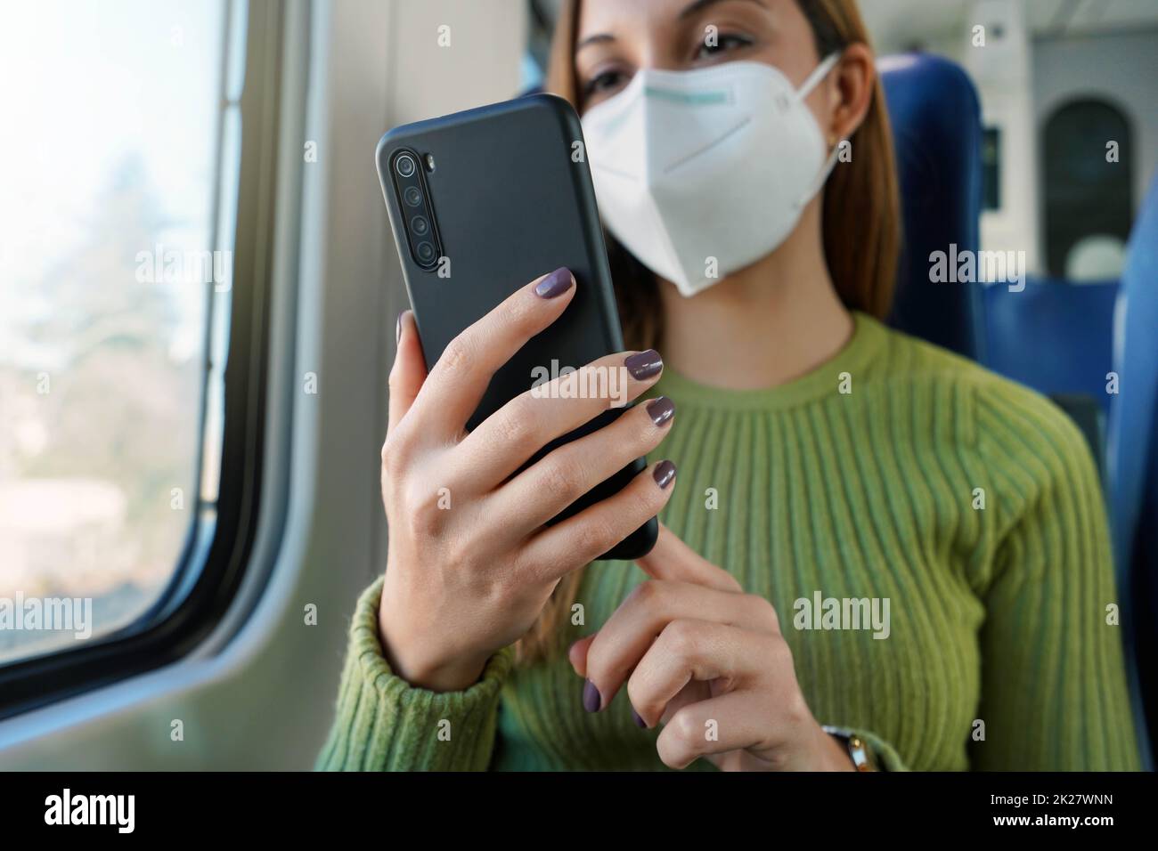 Trainieren Sie den Passagier mit der Smartphone-App während der Fahrt zur Arbeit und tragen Sie eine Gesichtsmaske. Konzentrieren Sie sich auf das Telefon. Stockfoto