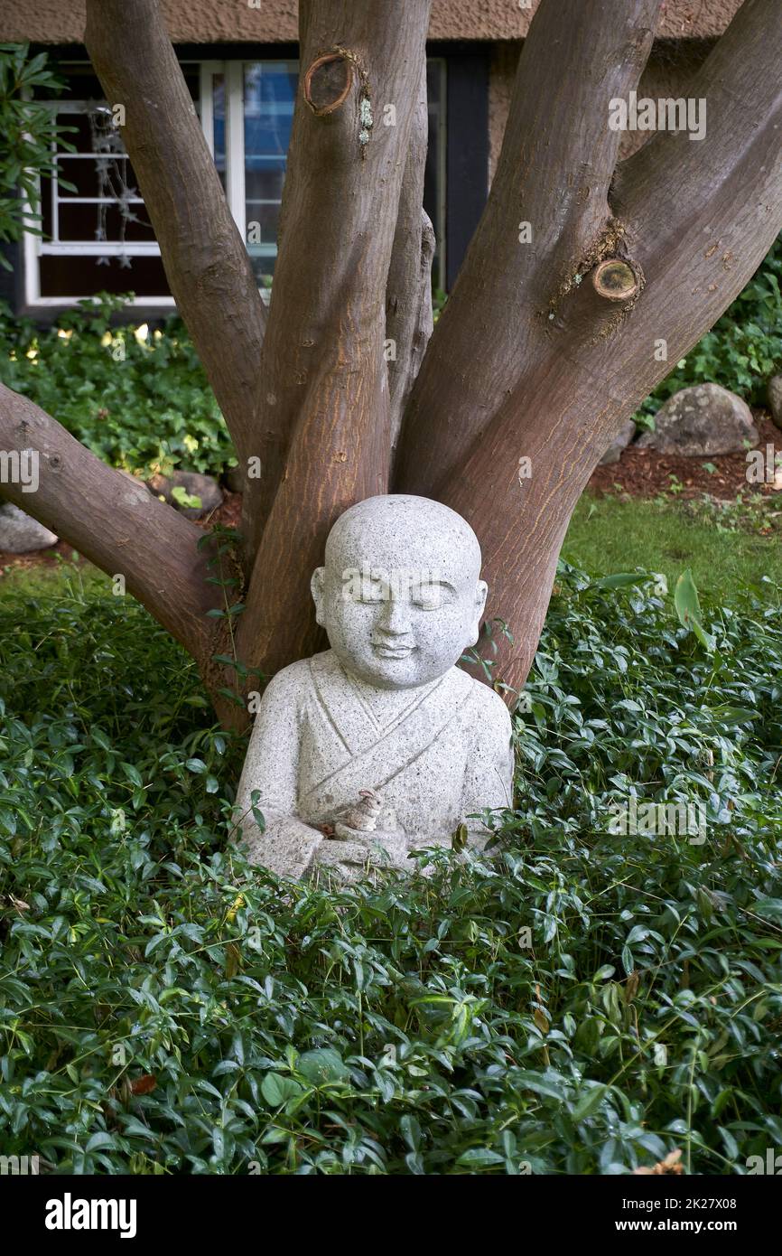 Granitskulptur eines Buddha und eines Hasen, die unter einem Baum inmitten von Grün sitzen Stockfoto