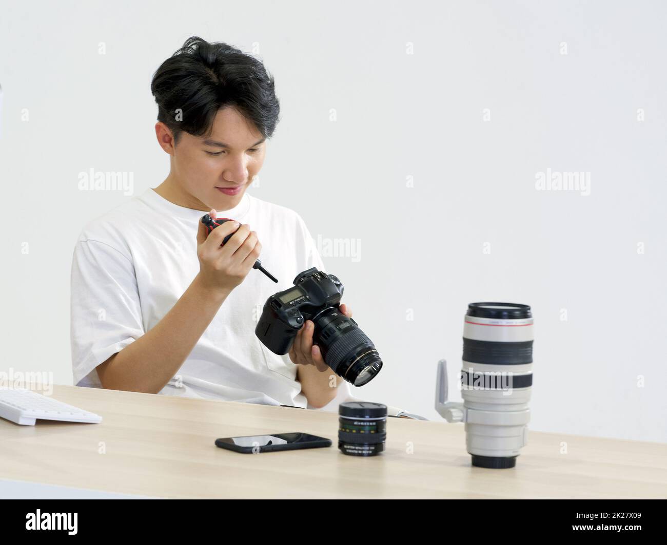 Der junge asiatische Fotograf putzt den Kamerabildschirm und den Körper mit einer Gebläsekamera, um ihn auf seinem Schreibtisch zu reinigen. Stockfoto