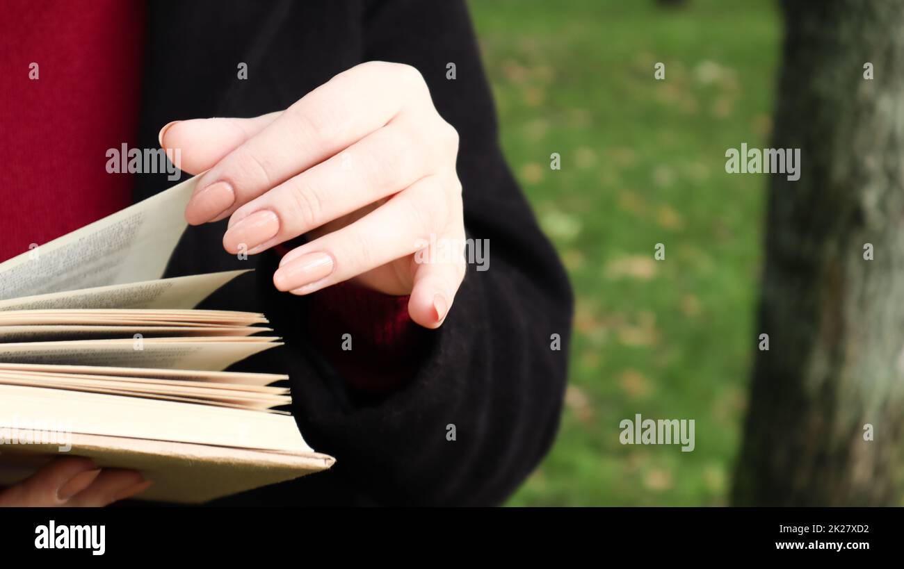 Ein Mädchen liest im Park ein Buch. Weibliche Hände, die im Freien Seiten von Papierbüchern umblättern. Der Schüler bereitet sich auf die Prüfung vor. Literarische Freizeitaktivitäten in der Natur. Nahaufnahme, Kopierbereich. Stockfoto