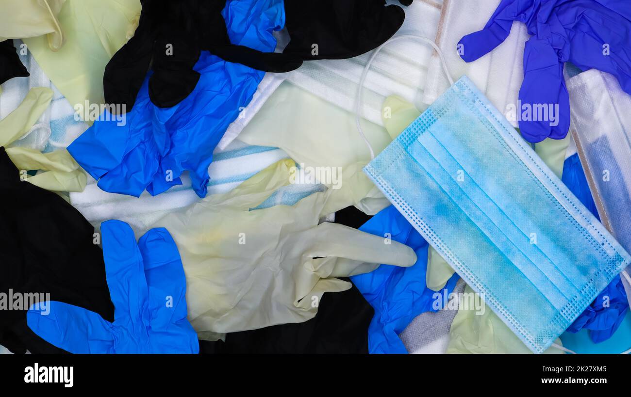 Mehrfarbige zerknitterte Latex-Operationshandschuhe und medizinische Schutzmasken liegen im Chaos. Flach verlegt. Verwendete Mittel gegen das Covid-19-Virus Stockfoto