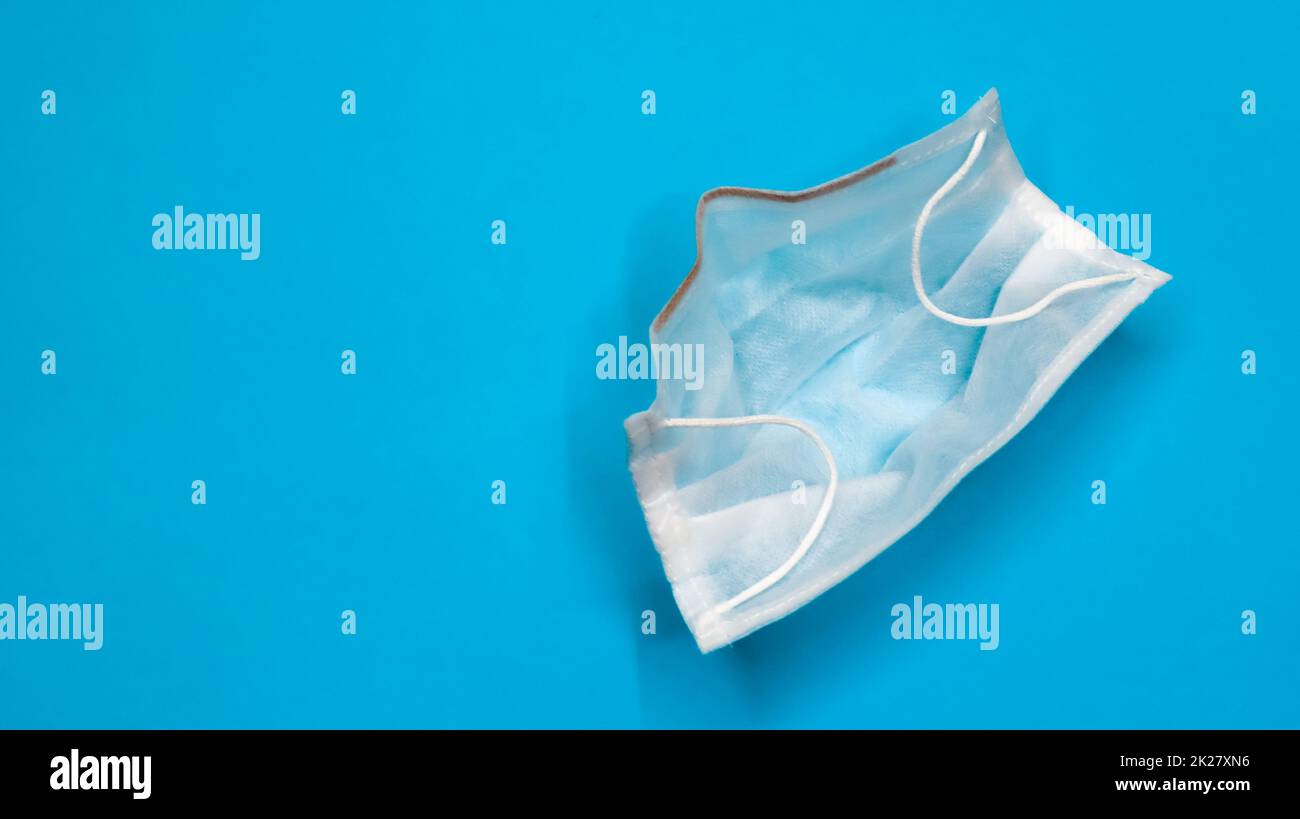 Eine 3-lagige chirurgische Einweg-Gesichtsmaske mit Gummipolstern, die Mund und Nase vor blauem Hintergrund bedecken. Das Konzept des Bakterienschutzes, des Gesundheitswesens und der Medizin. COVID-19. Speicherplatz kopieren Stockfoto
