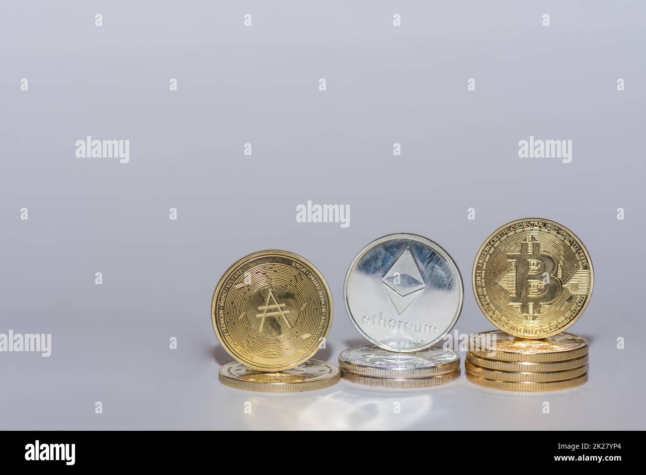 Wertvolle Kryptomünzen Bitcoinäther und ada in einer Reihe mit Grau Stockfoto