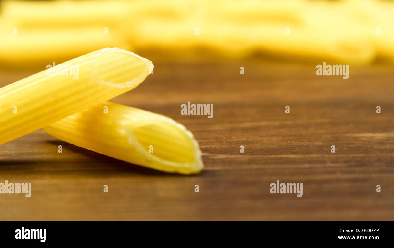 Penne Rigate Raw Pasta ist eine kurze Pasta mit schrägen Schnitten und einer gerippten Oberfläche. Traditionelle italienische Pasta. Nudelhintergrund. Seitenansicht der italienischen Speisezutat auf dem braunen Tisch. Speicherplatz kopieren Stockfoto