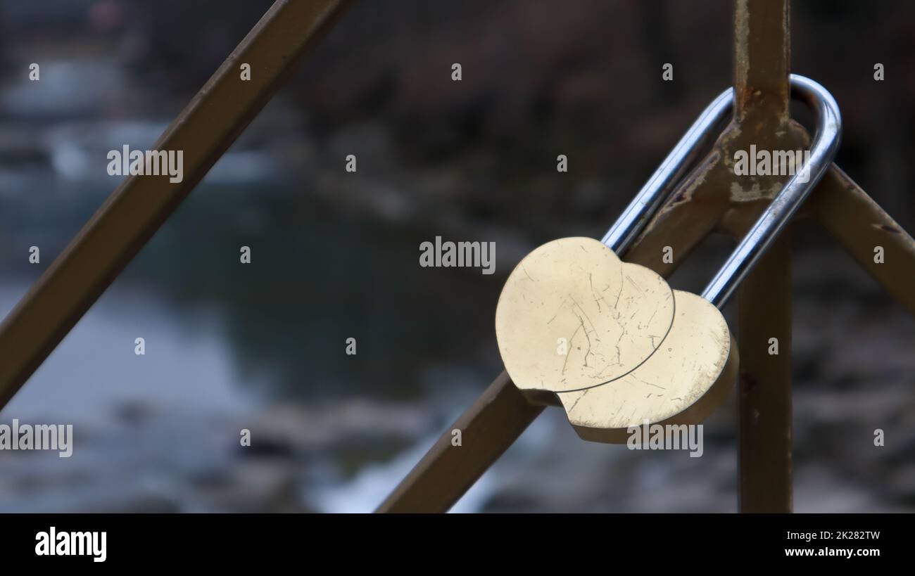 Ein Schloss aus verflochtenen Herzen, auf einem Geländer eingeschlossen als Zeichen ewiger Liebe. Zwei Herzen in Form einer gelben Burg der Liebe, die auf dem Geländer der Brücke hängt Stockfoto