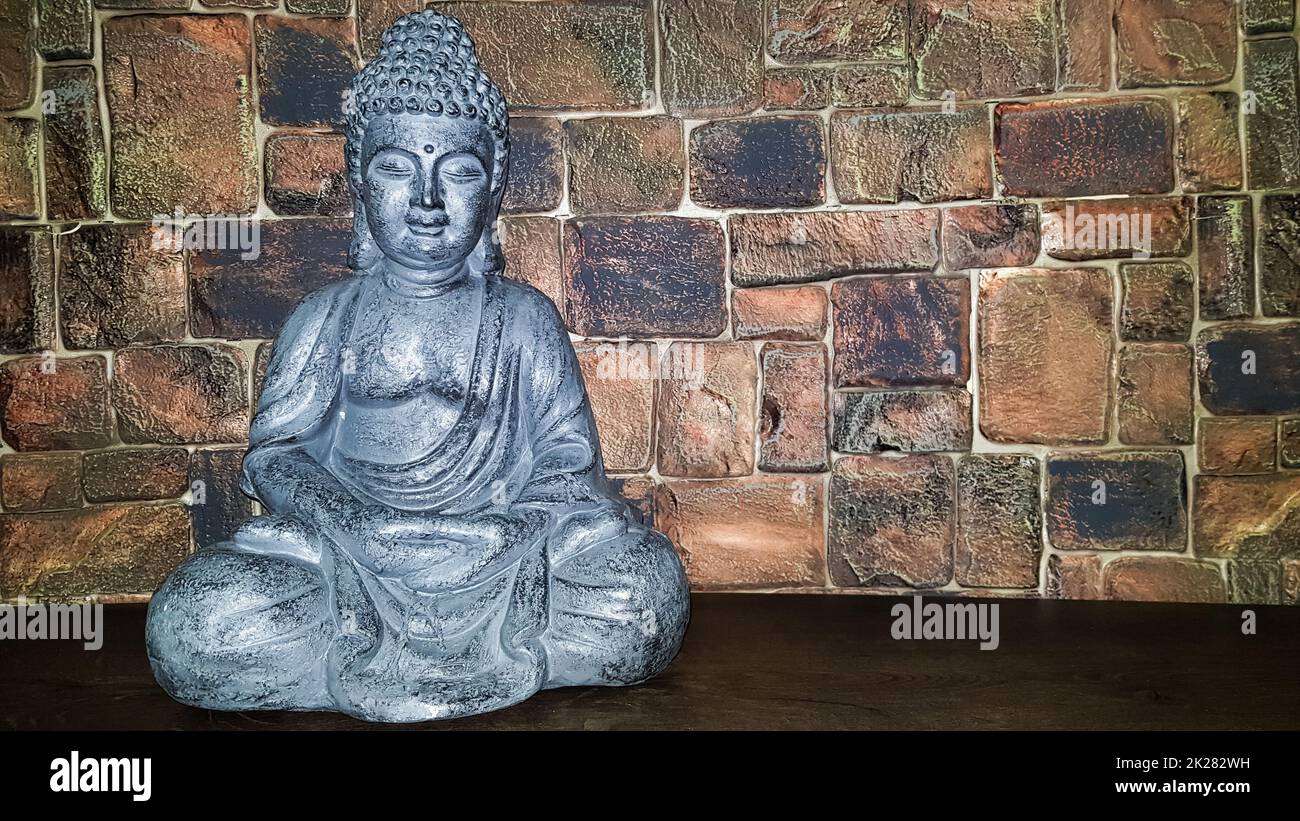 Ukraine, Kiew - 10. Juni 2020. Statuette des Segens Buddhas auf einem hölzernen Regal vor einer Steinmauer. Keramikfiguren und -Figuren Dekoration oder Symbol im Innenraum. Stockfoto