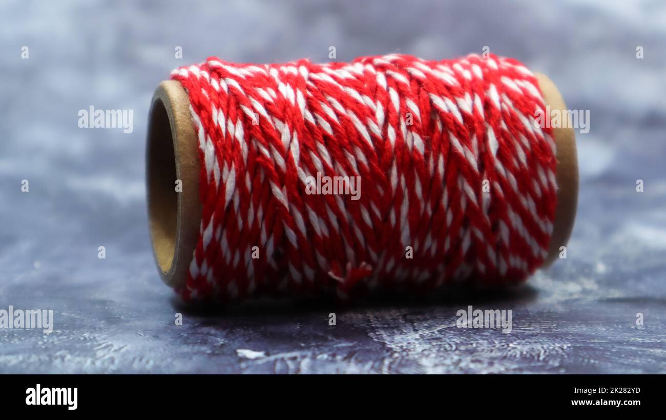 Bäckerschnur. Rote und weiße Linien. Rote Rolle Wollfaden, Nahaufnahme auf grauem Marmorhintergrund. Spule mit dekorativen Gewinden. Stockfoto