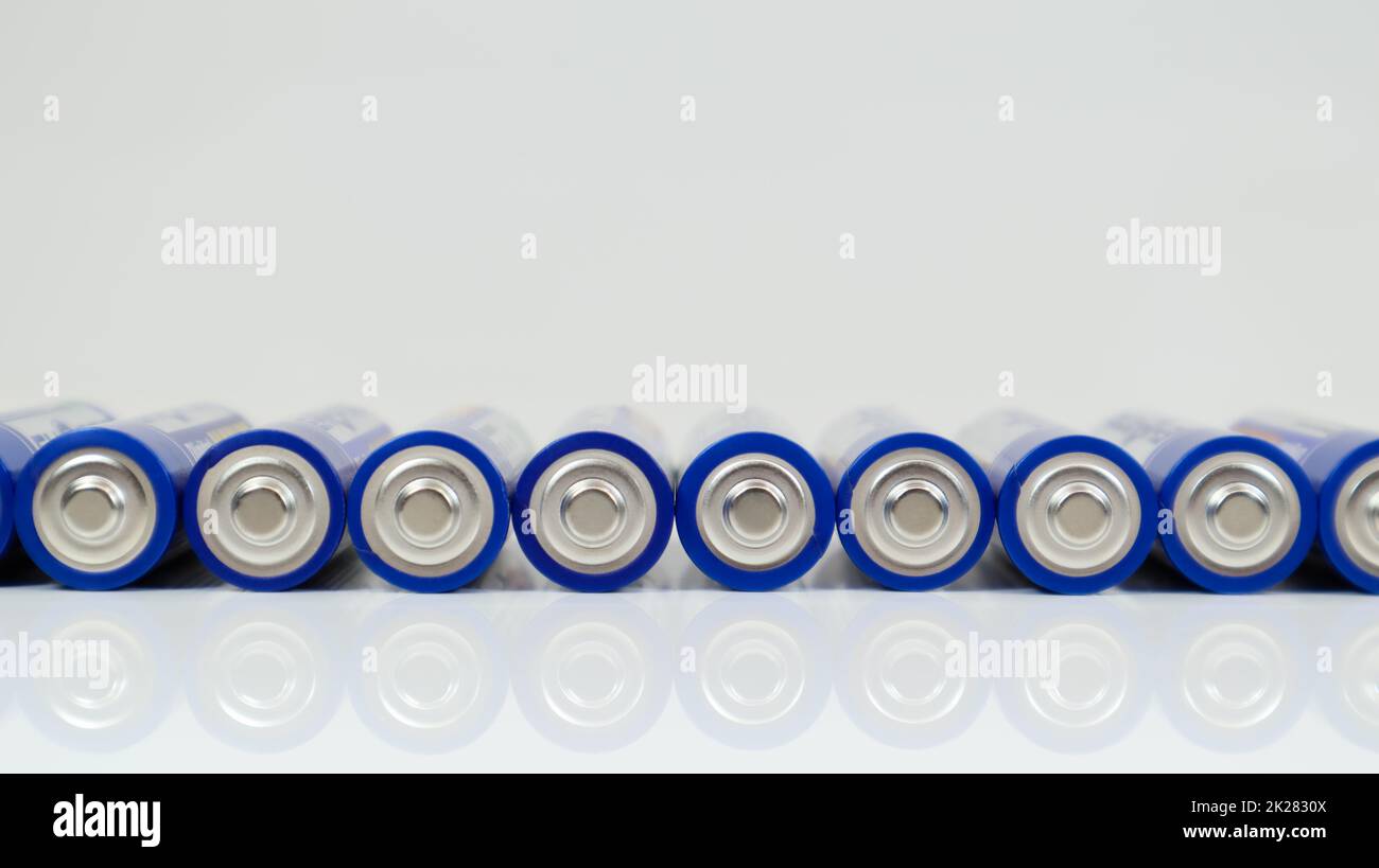 Viele AA-Alkali-Batterien auf weißem glänzendem Hintergrund mit Reflexion und einer Reihe angeordneter Kopien. Stockfoto