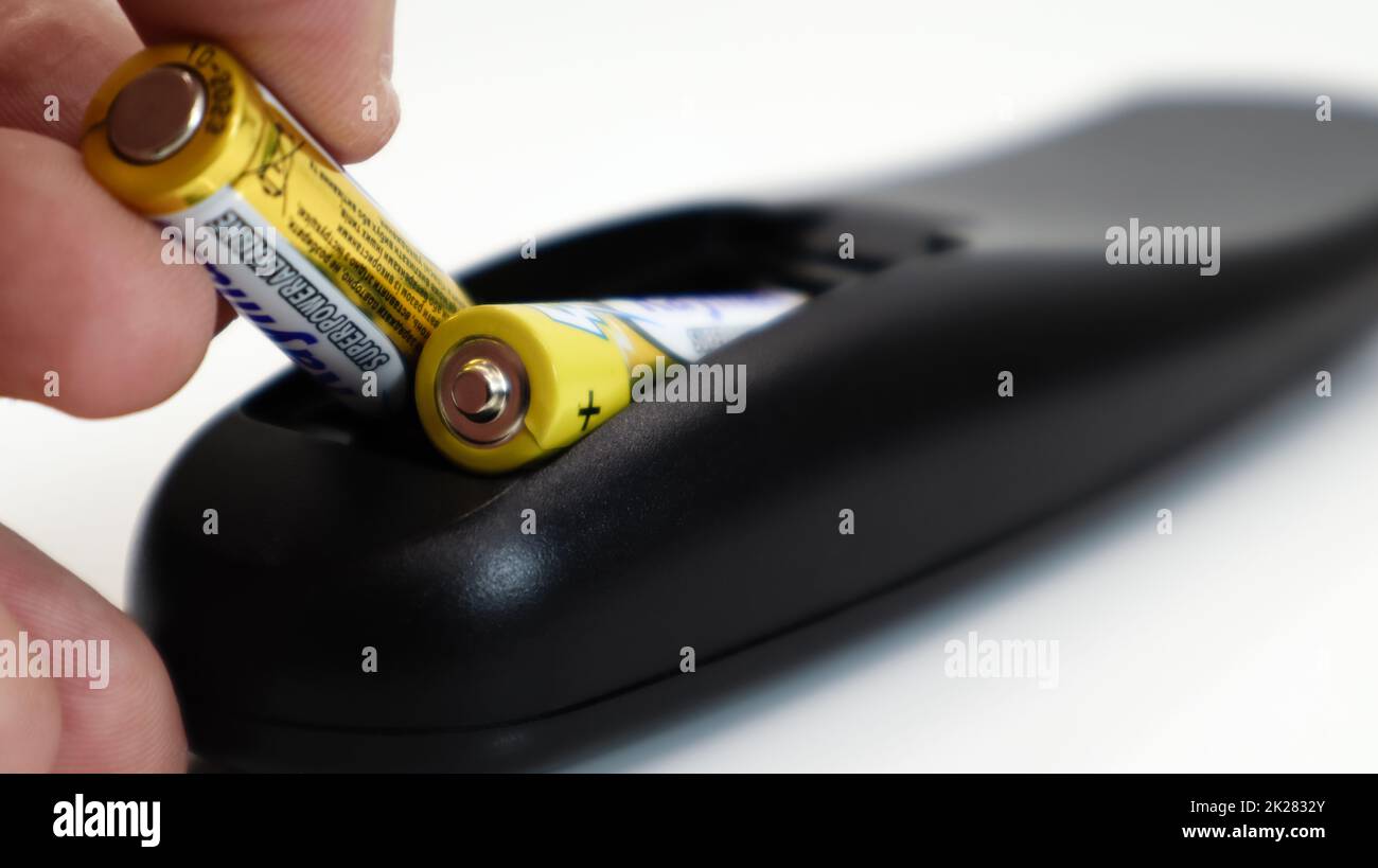 Setzen Sie die AAA-Batterie in die Fernbedienung ein. Einlegen der  Batterien in das drahtlose Gerät. Eine gelbe Alkali-Mangan-Batterie  befindet sich in der Hand eines Mannes. Text in Englisch und Russisch  Stockfotografie 
