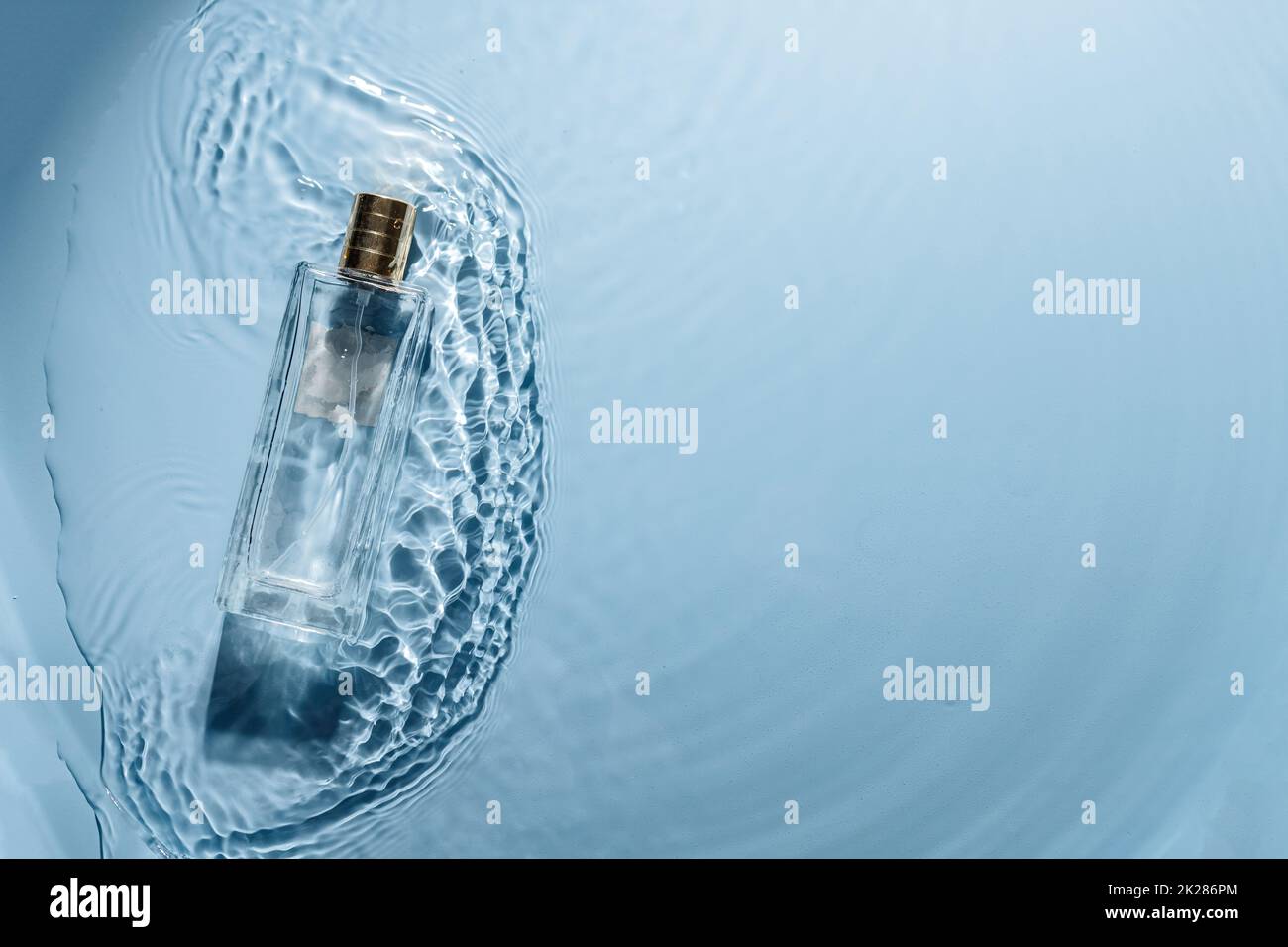 Parfüm-Flasche auf blauem Wasser welligen Hintergrund. Frisches Meeresduft-Konzept. Frauen- und Männeressenz Stockfoto