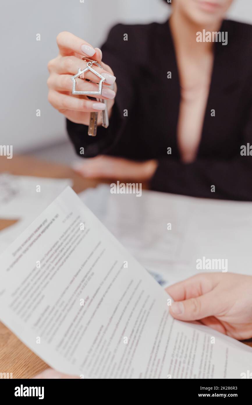 Die junge maklerin überreicht die Schlüssel für die Immobilie, der Kunde liest den Vertrag. Vermietung und Kauf von Immobilien Stockfoto