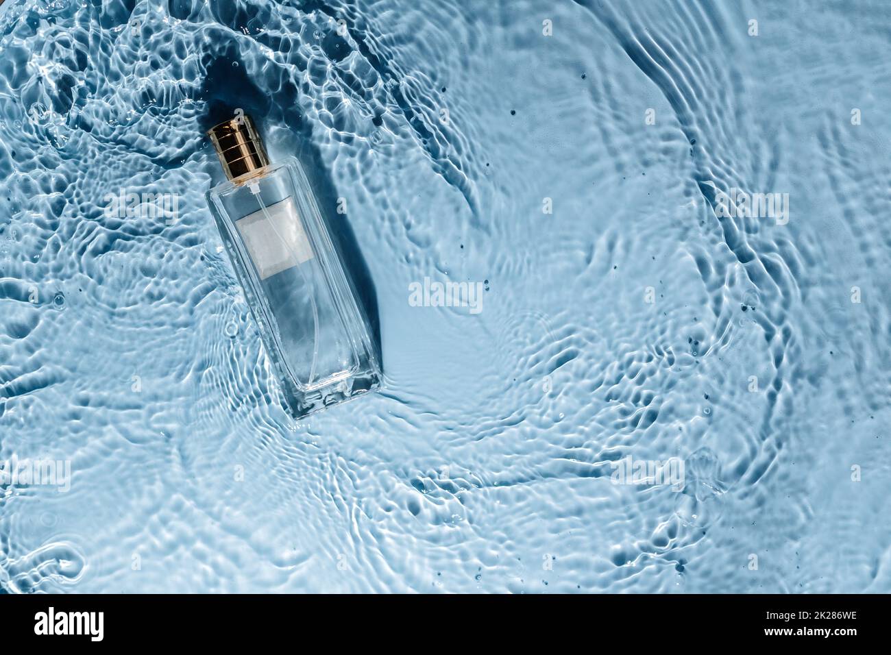 Parfüm-Flasche auf blauem Wasser welligen Hintergrund. Frisches Meeresduft-Konzept. Frauen- und Männeressenz. Stockfoto