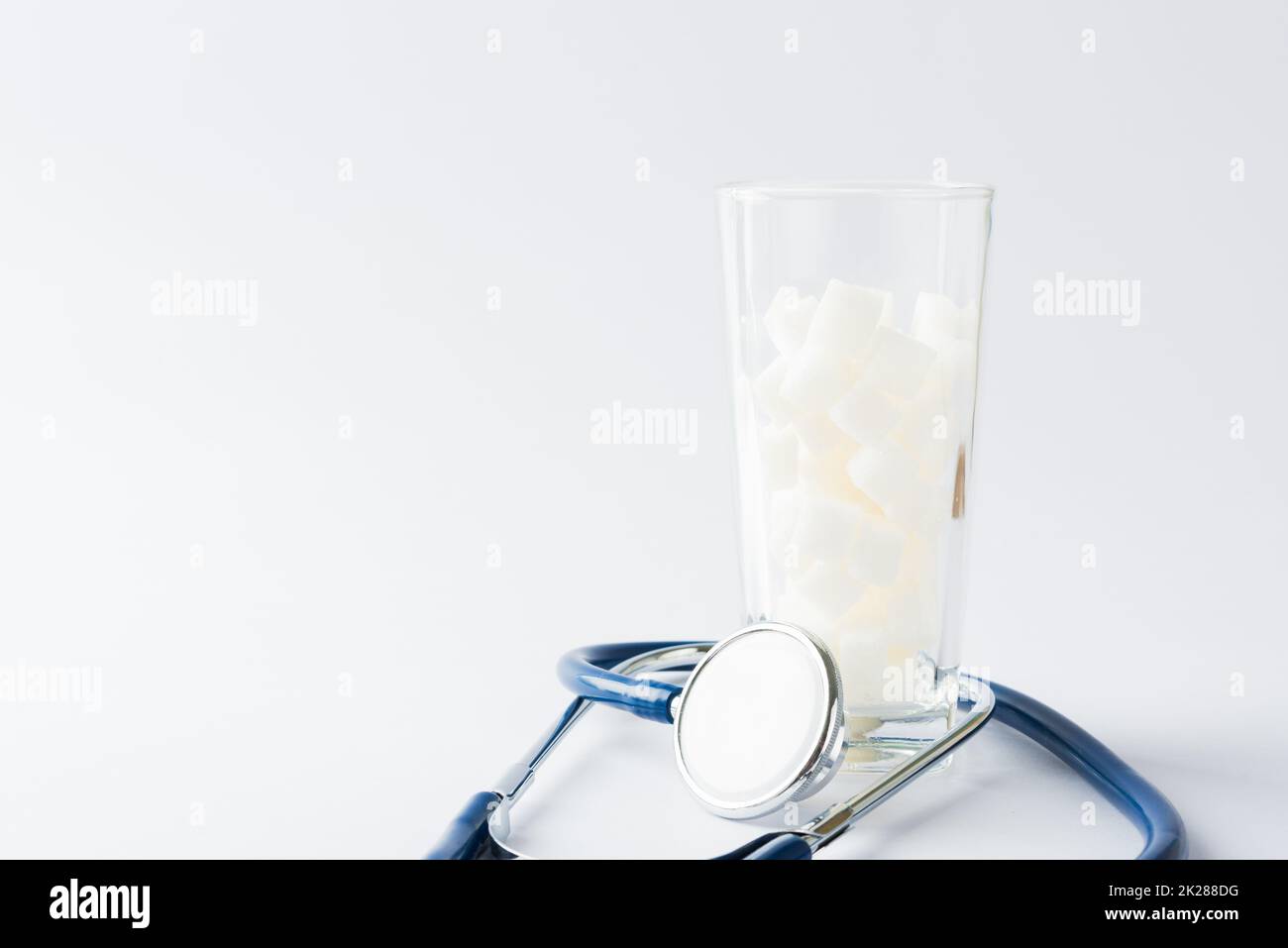 Glas voll von weißem Zucker Würfel süße Lebensmittel Zutat und Arzt Stethoskop Stockfoto