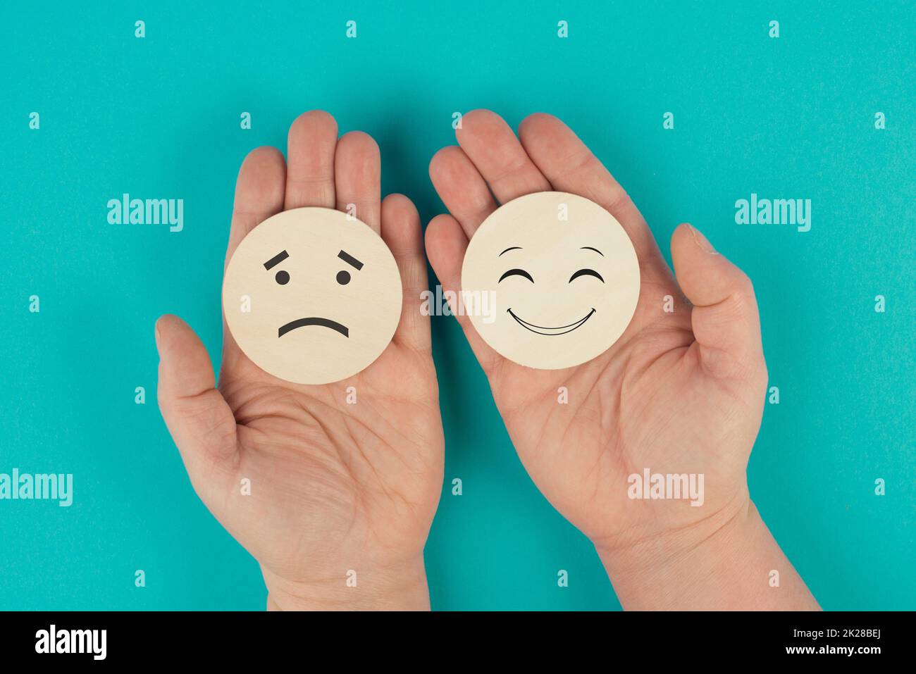Zwei hölzerne Kreise in den Händen zu halten, ist ein Gesicht traurig, das andere lächelt, porsitive und negative Emotionen, Bewertungskonzept, Stimmungswahl Stockfoto