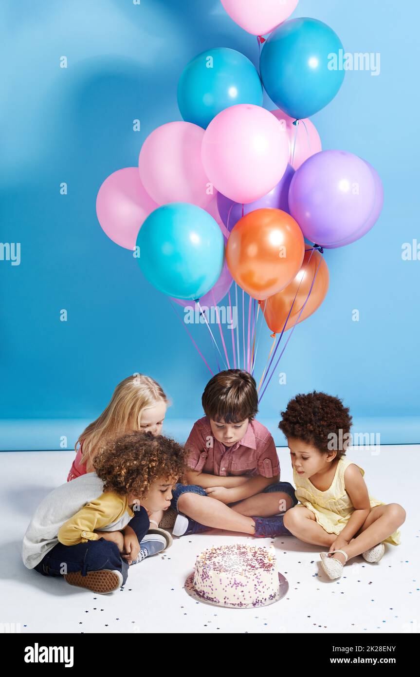 Wunsch nach einem Ballon. Eine Gruppe von Kindern blasen die Kerzen auf einem Geburtstagskuchen. Stockfoto