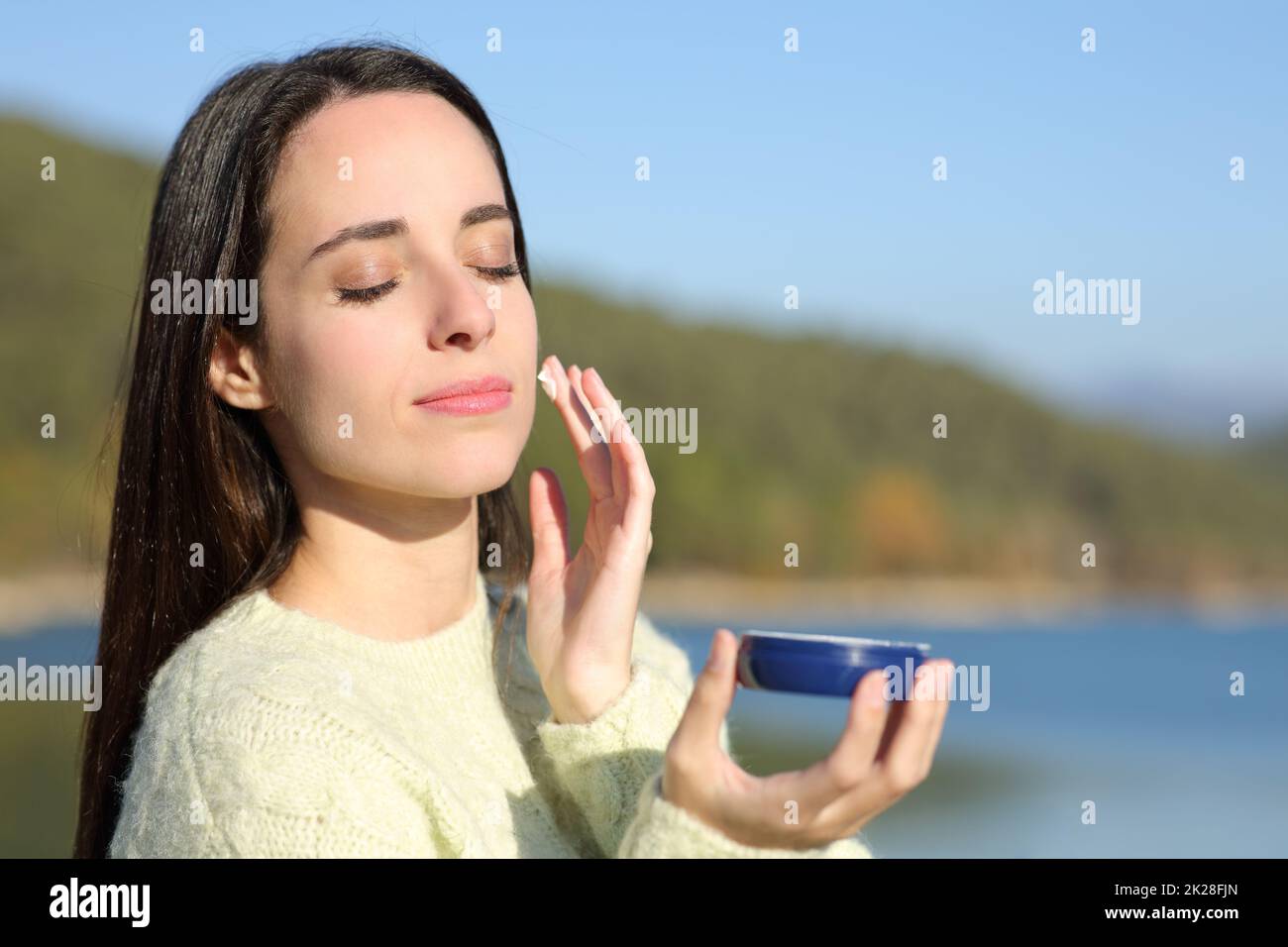 Frau, die Feuchtigkeitscreme auf das Gesicht in einem See aufträgt Stockfoto