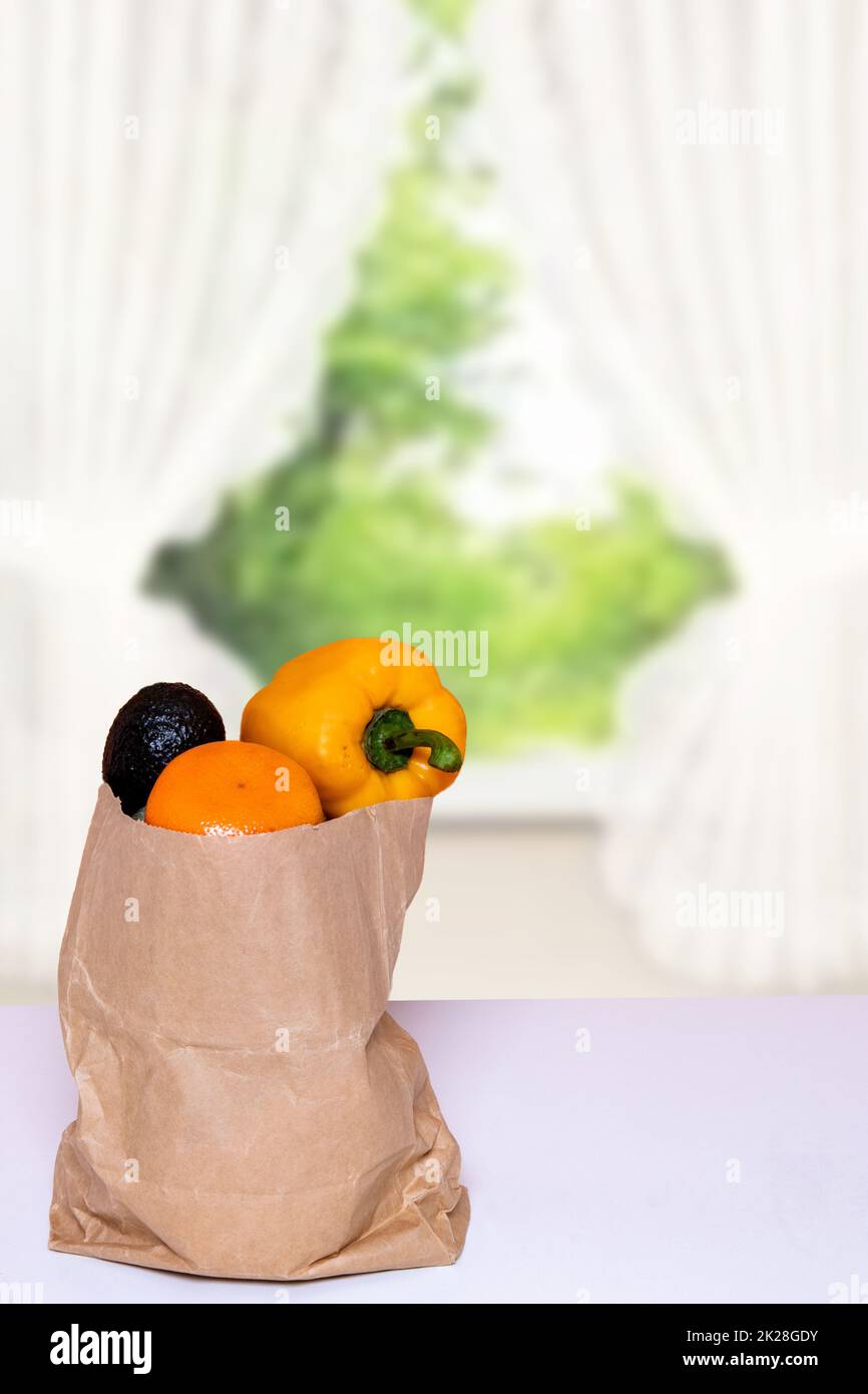 Nahaufnahme einer braunen Einkaufstasche aus Papier mit frischem Gemüse auf dem Tisch über einem verschwommenen abstrakten Vorhanghintergrund. Platz für die Montage der Produktpräsentation. Konzept der Stärkung des Immunsystems. Stockfoto