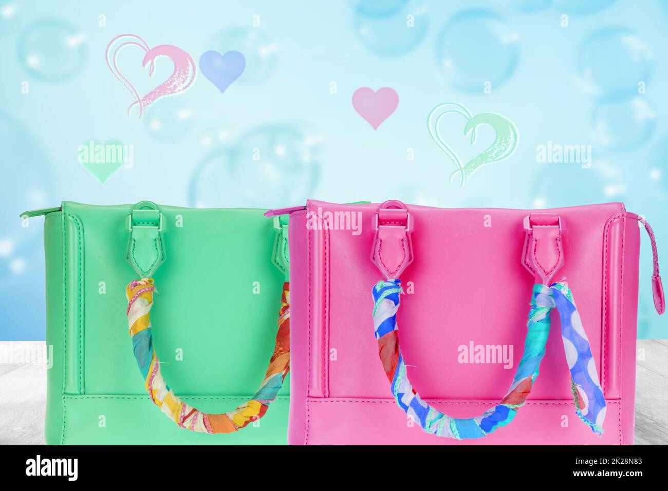 Vorlage „Happy Valentines or Mothers Day“. Eine schöne grüne und pinkfarbene Damenhandtasche, dekoriert mit einem farbenfrohen Tuch auf dem Tisch auf abstraktem blauem Herzhintergrund. Stockfoto