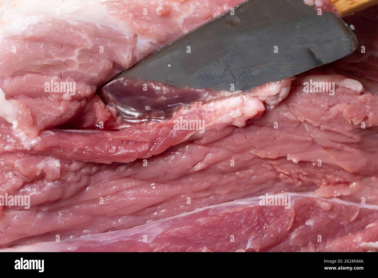 Schneiden Sie das Schweinefleisch oder Rindfleisch mit einem Messer auf dem Tisch in Nahaufnahme. Zubereitung von Fleischgerichten und Nahrungsmitteln. Stücke von rotem Fleisch für Shish Kebab, Barbecue oder Kebab. Rohes frisches Fleisch wird mit einem Messer geschnitten. Rezept Stockfoto