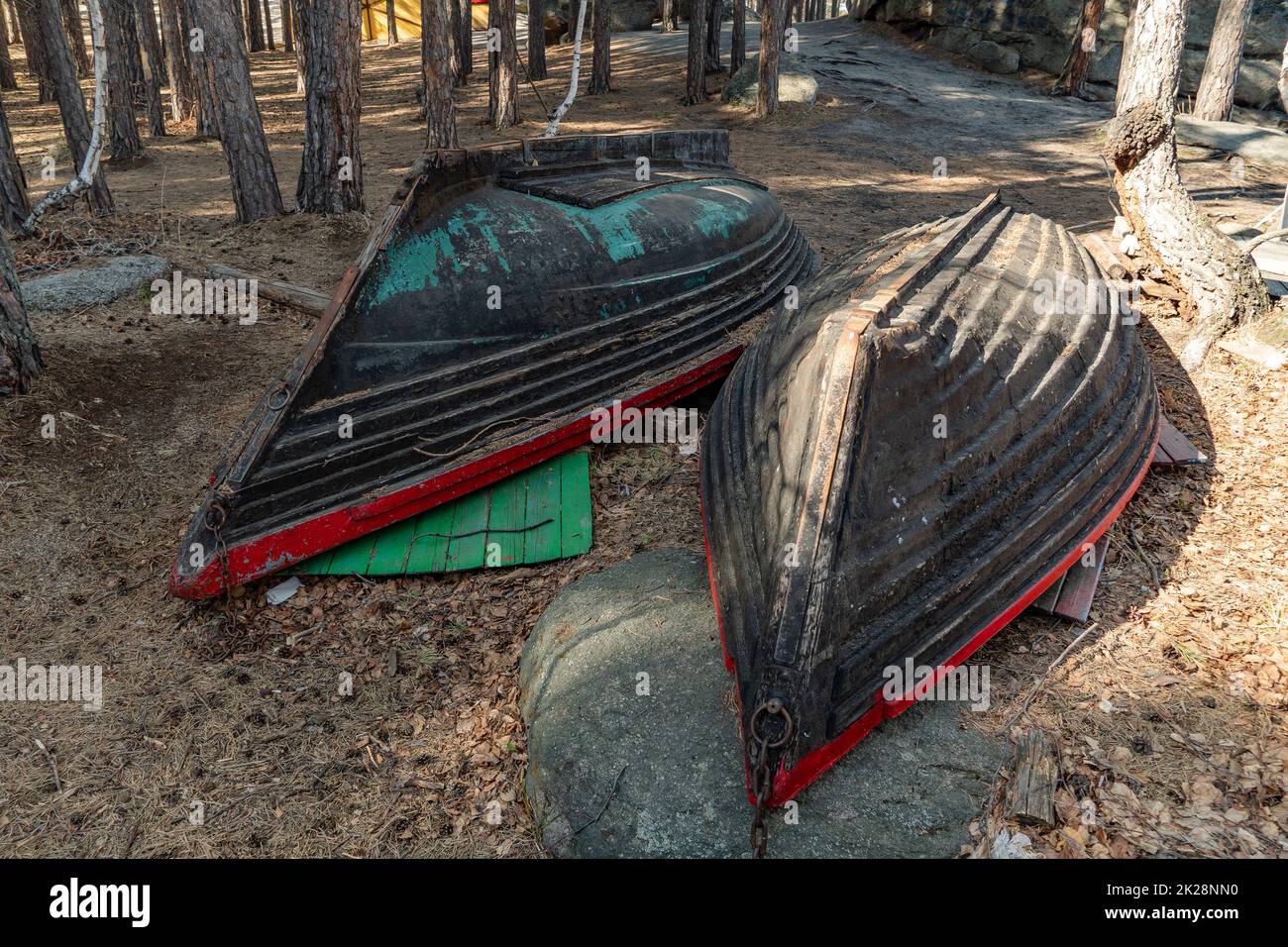 Zwei alte Fischerboote liegen am Ufer des Bergseeufers im Wald. Umgedrehte Holzboote auf dem Küstenstreifen oder der Küste. Küstenlinie Stockfoto