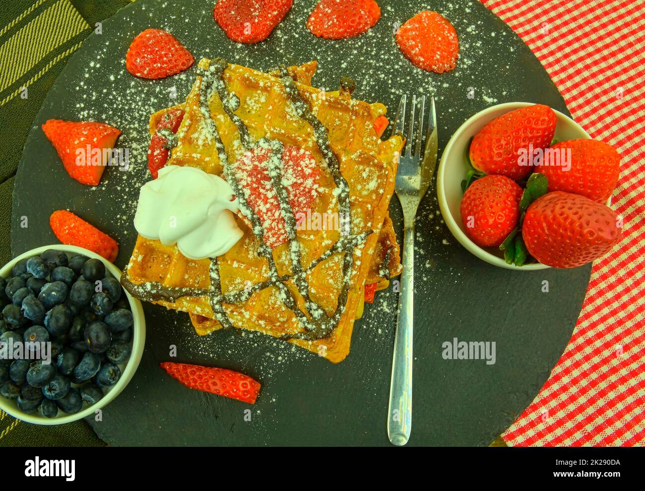 Traditionelle belgische Waffeln mit Heidelbeeren und Erdbeeren. Geschmolzene Schokolade und Schlagsahne auf Waffeln. Draufsicht. Schwarzer Schieferhintergrund. Stockfoto