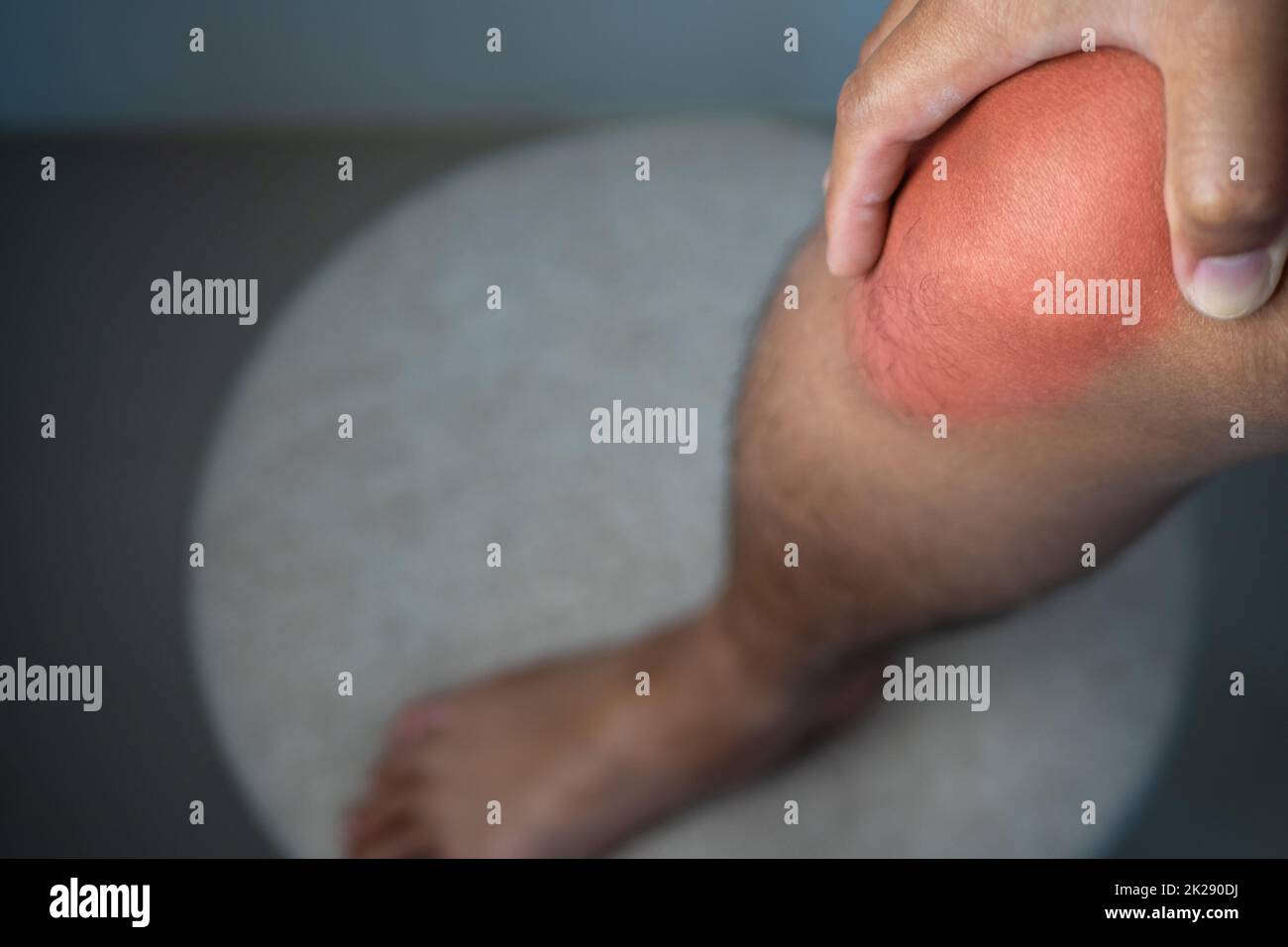 Der Mann hält seinen Schmerzpunkt am Kniegelenk. Der rote Punkt zeigt die Verletzungsposition an. Stockfoto