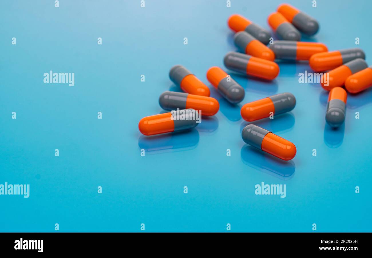 Orange-graue Antibiotikakapseln auf blauem Hintergrund. Antibiotikaresistenz. Pharmazeutische Industrie. Verschreibungspflichtige Medikamente. Herstellung von Kapselpillen. Pharmakologie und Toxikologie. Stockfoto