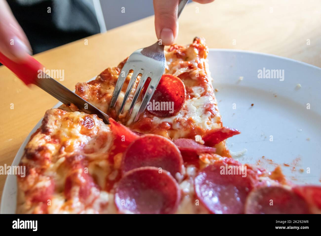 Junge Hände schneiden Salami-Pizza in Stücke mit Gabel und Messer auf Pizzateller in Nahaufnahme Makroansicht mit köstlichem Käse und Salami als fettes, ungesundes Fast Food für hungrige Teenager, italienische Delikatessen Diät Stockfoto