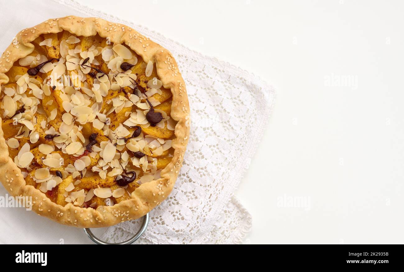 Gebackener, runder Kuchen mit Apfelstücken, mit Mandelflocken bestreut auf einem weißen Tisch Stockfoto