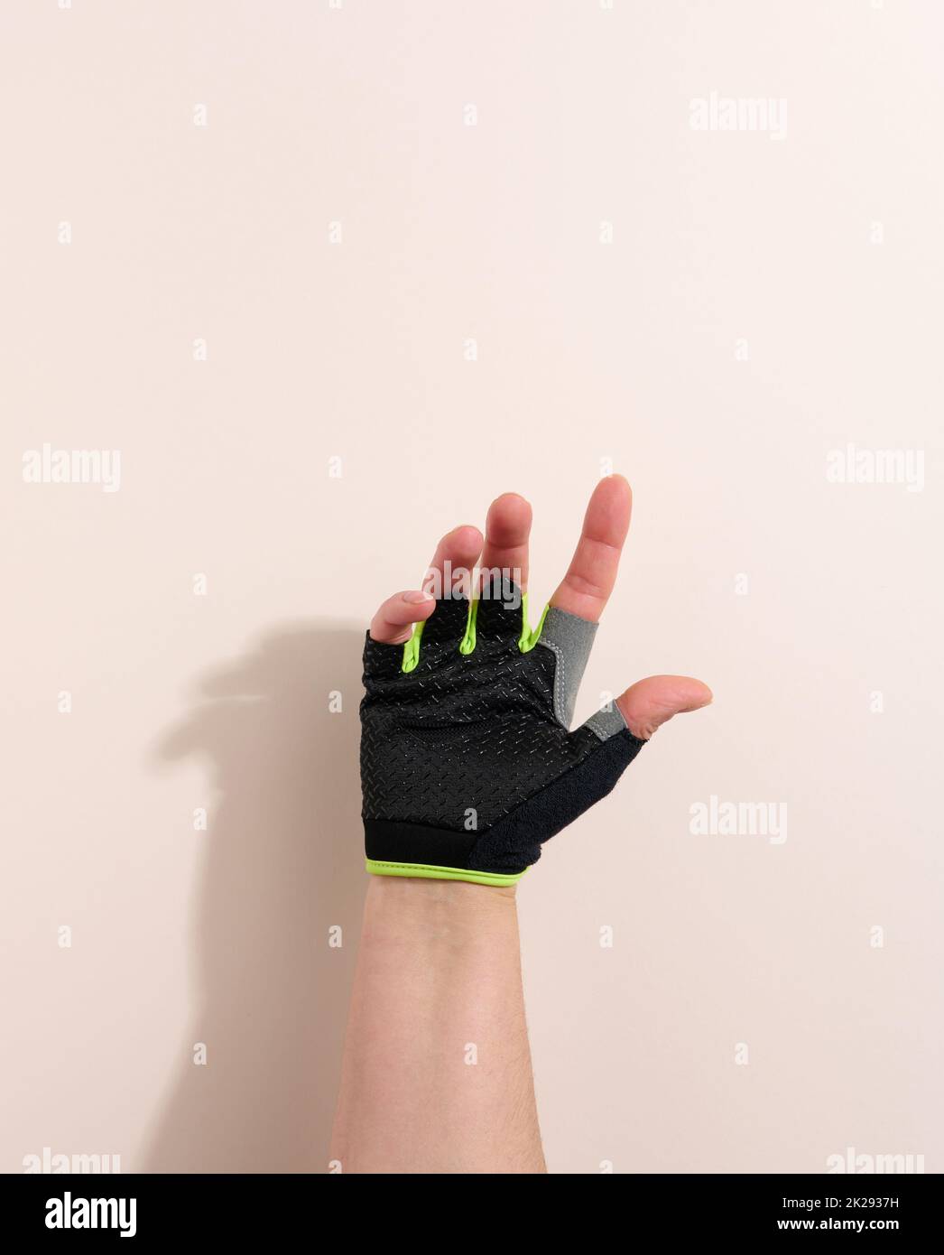 Schwarzer Sporthandschuh auf weiblicher Hand, beiger Hintergrund. Ein Teil des Körpers wird angehoben Stockfoto