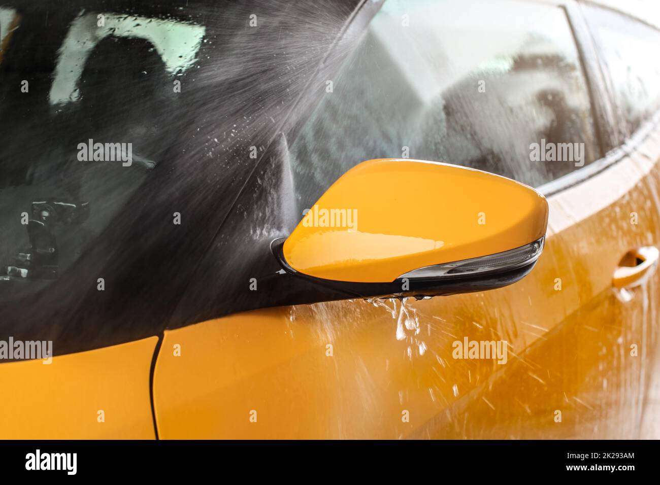 Seite Spiegel der gelben Auto in Self-Service-Autowaschanlage gewaschen wird, Wasser sprühen mit hohem Druck, Tropfen fliegen herum. Stockfoto