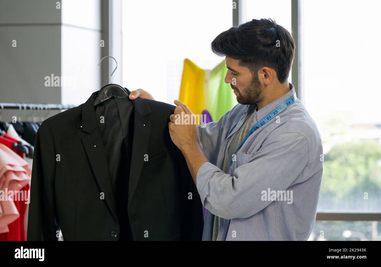 Modedesigner-Zimmer. Die Schneiderin der Herren verwendet eine Nadel, um zu markieren, wo die Knöpfe auf einem schwarzen Anzug geknöpft werden. Stockfoto