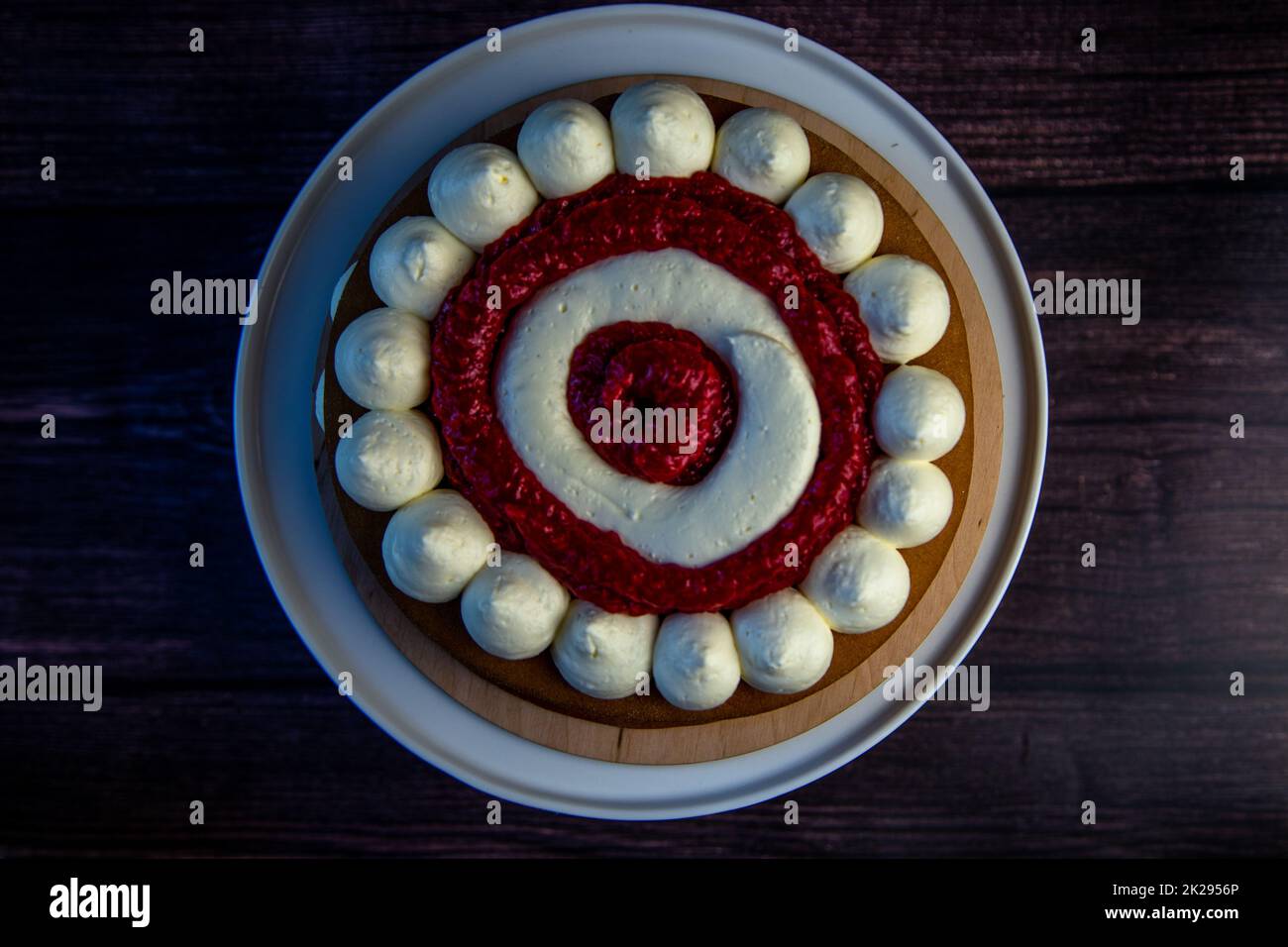 Ein Kuchen mit weißen Cremekreisen, abwechselnd mit Himbeermarmelade auf dunklem Hintergrund, Draufsicht, Nahaufnahme Stockfoto